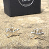 Silver 'X' shaped earrings on a textured surface with a black box labelled Fred & Emily' in the background.