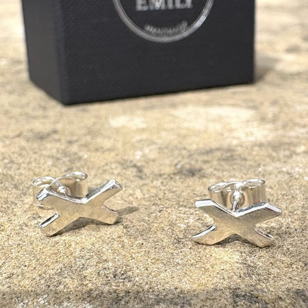 Silver 'X' shaped earrings on a textured surface with a black box labelled Fred & Emily' in the background.