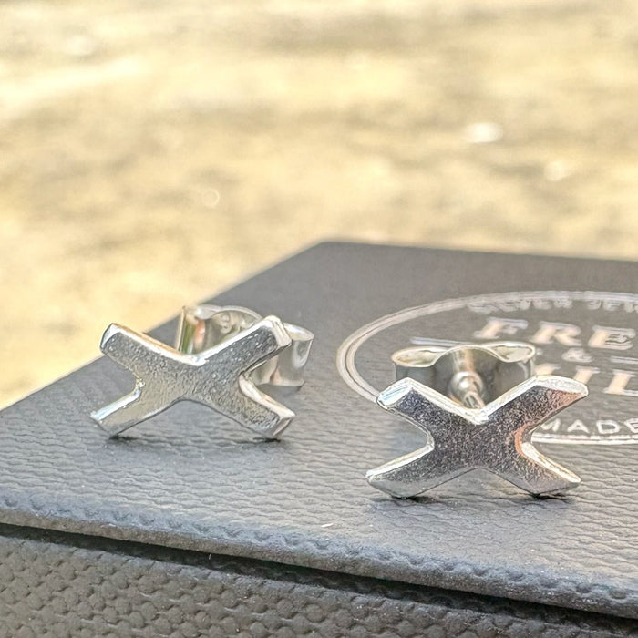 Silver 'X' shaped earrings on a grey textured surface, kiss earrings