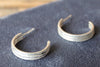 Pair of silver hoop earrings on a dark fabric background