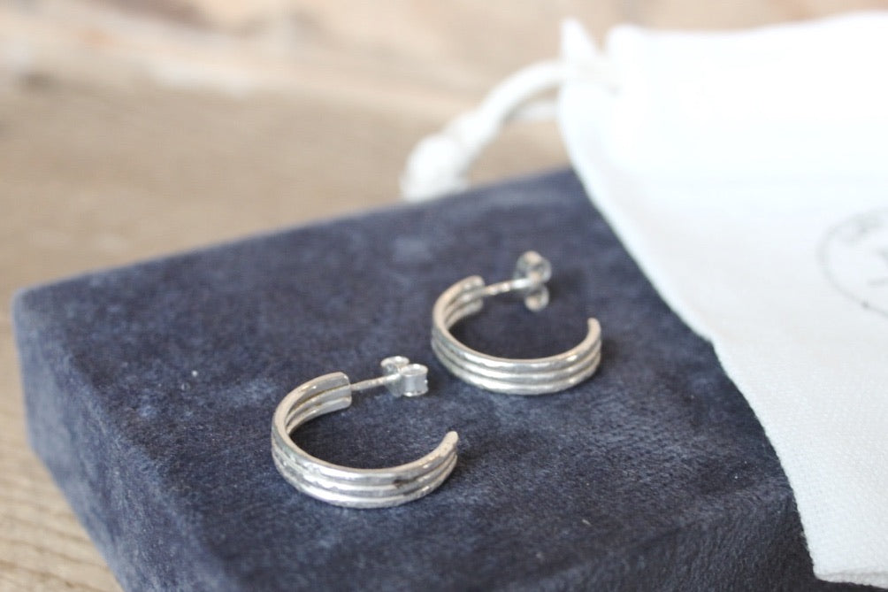 Pair of silver hoop earrings on a blue cushion with a blurred background