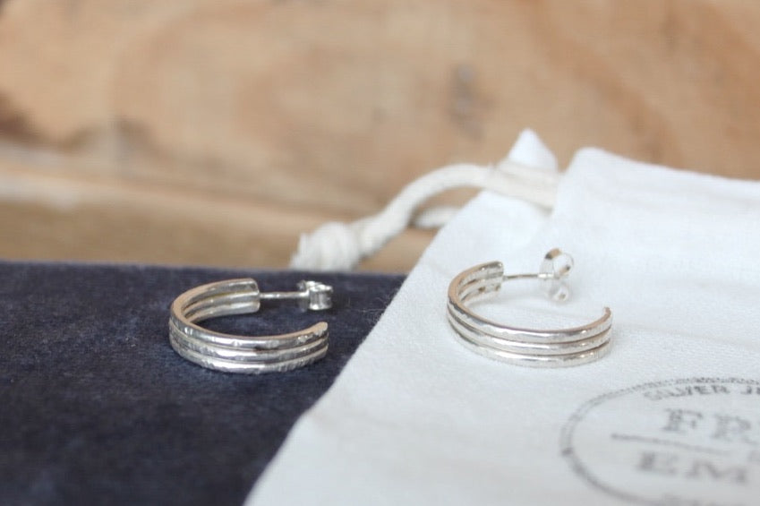Silver hoop earrings on a F&E branded jewellery pouch with a blurred wooden surface in the background.