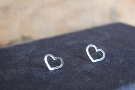 two small silver heart earrings studs sat on a blue background