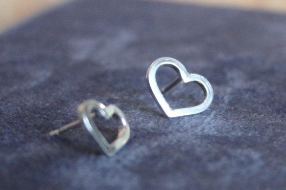 two small silver heart earrings studs sat on a blue background