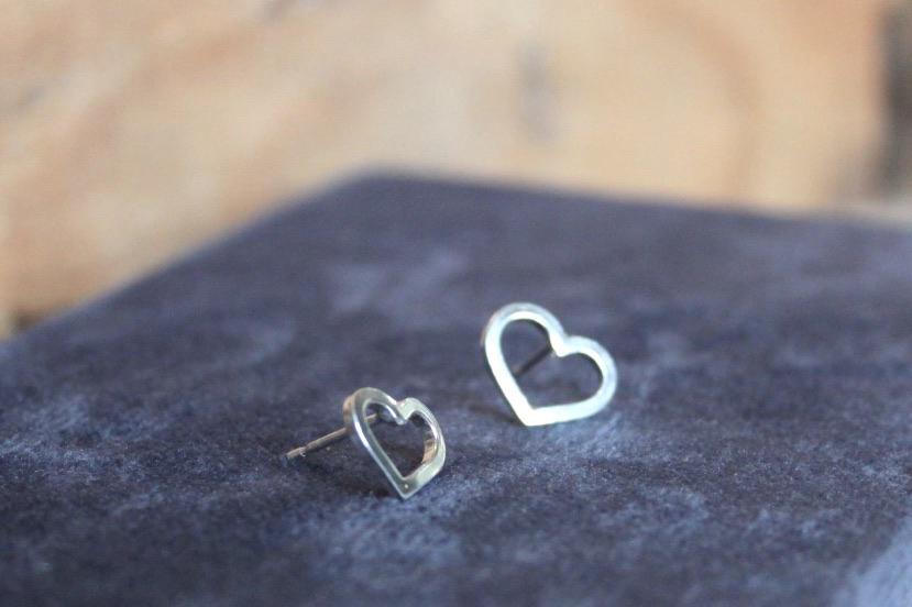 two small silver heart earrings studs sat on a blue background
