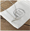 A silver T bar necklace with a hammered finish, laid on a belcher chain on a white linen bag..