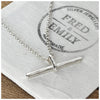 A silver T bar necklace with a hammered finish, laid on a belcher chain on a white surface.