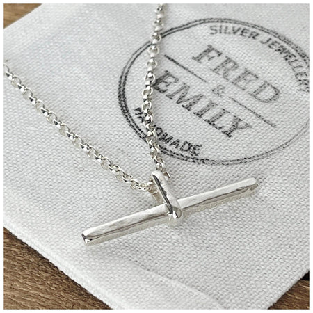 A silver T bar necklace with a hammered finish, laid on a belcher chain on a white surface.