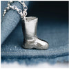 A silver wellington boot pendant on a chunky belcher chain, placed on a blue fabric surface.