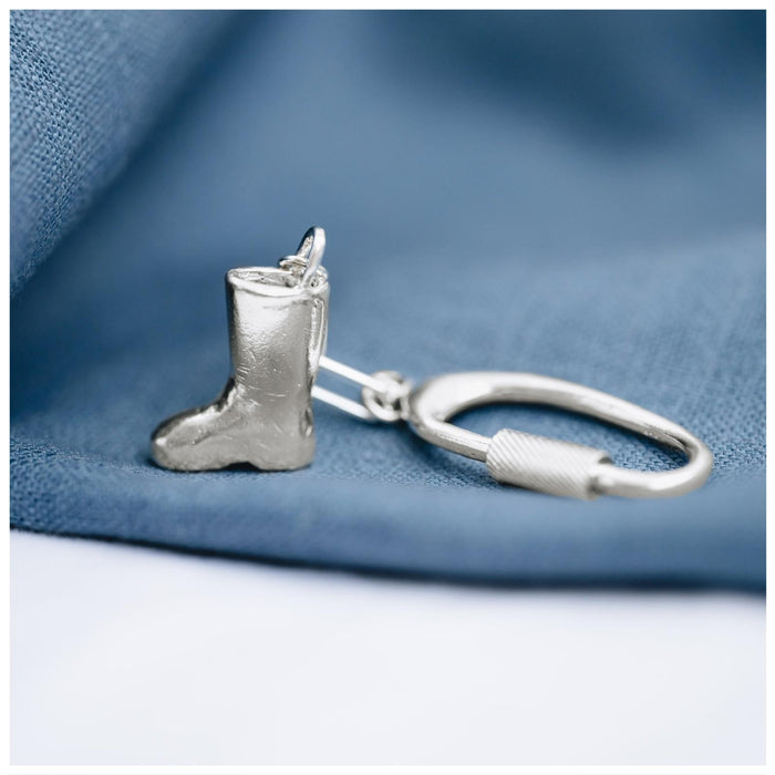 A sterling silver keyring in the shape of a handmade wellington boot on a blue textured background.