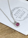 A sterling silver pendant with an oval pink tourmaline stone on an 18'' belcher chain, displayed on a white fabric with the brand mark 'FRED & EMILY'.