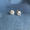 Sterling silver stud earrings with a bee on a piece of silver honeycomb sitting on a blue textured fabric background.