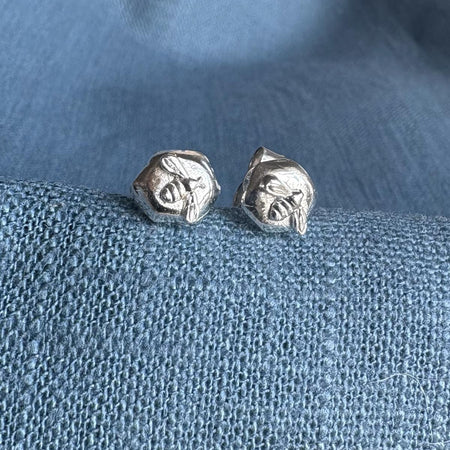 Sterling silver stud earrings with a bee on a piece of silver honeycomb sitting on a blue textured fabric background.