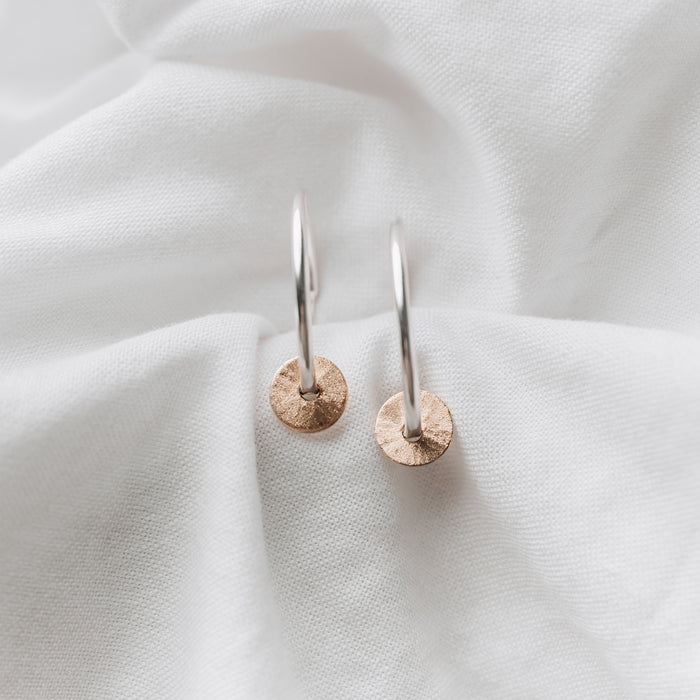 Silver hoops with a gold filled disc, textured to create a sparkle sitting on a white linen background