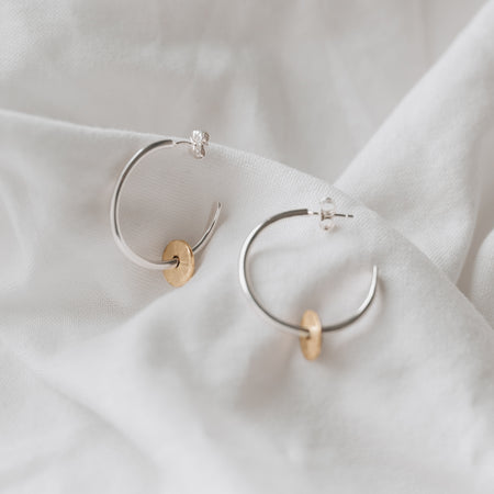 Silver hoops with a gold filled disc, textured to create a sparkle sitting on a white linen background