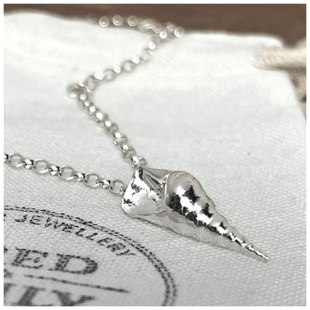 A sterling silver conch sea shell pendant hanging on a 2.5mm belcher chain, displayed against a white background with a Fred & Emily Stamp