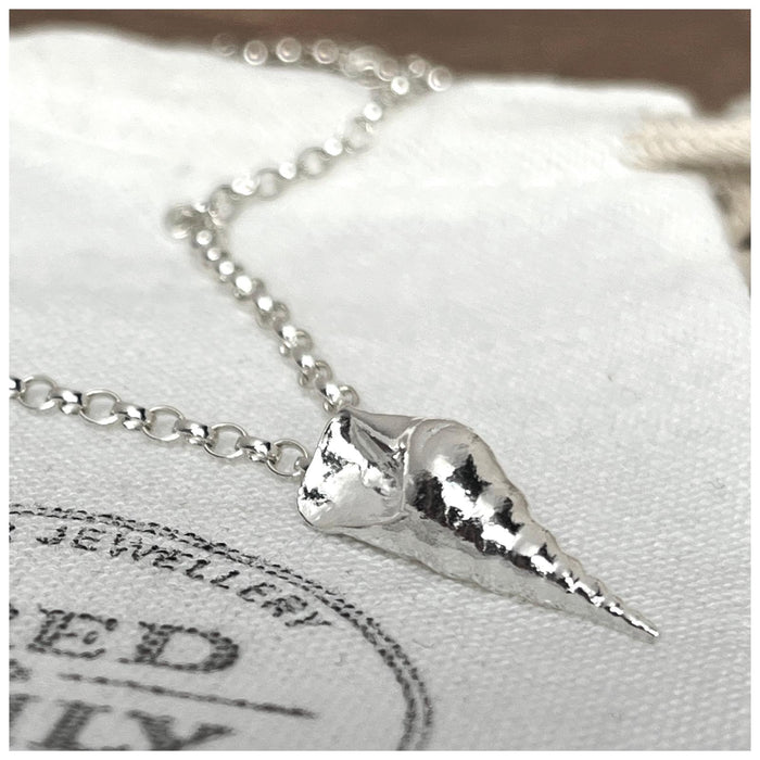 A sterling silver conch sea shell pendant hanging on a 2.5mm belcher chain, displayed against a white background with a Fred & Emily Stamp