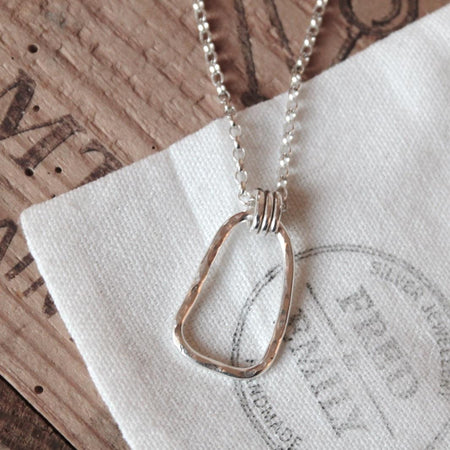 Silver necklace with an organic hoop help by three silver jump rings with a textured surface