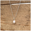 Small freshwater pearl pendant hanging from a silver chain on a wooden background