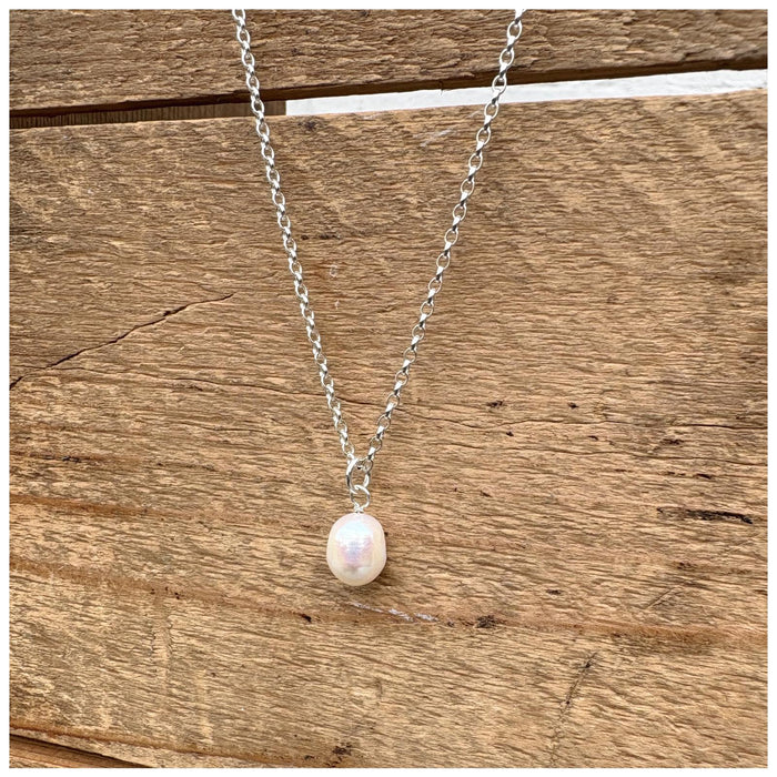 Small freshwater pearl pendant hanging from a silver chain on a wooden background