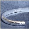 A solid sterling silver cuff bracelet with a hammered effect, showing the hallmarks on the inside of the bracelet.