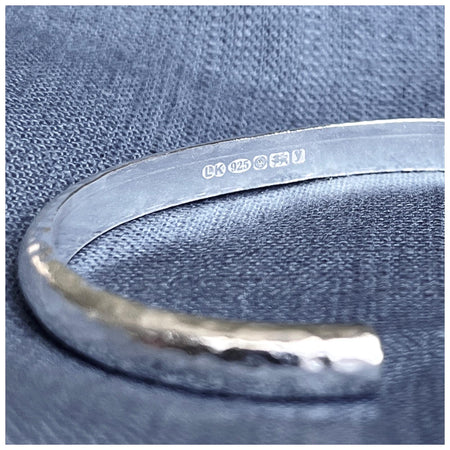A solid sterling silver cuff bracelet with a hammered effect, showing the hallmarks on the inside of the bracelet.