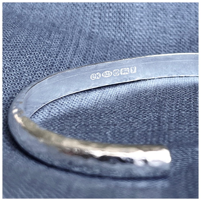 A solid sterling silver cuff bracelet with a hammered effect, showing the hallmarks on the inside of the bracelet.