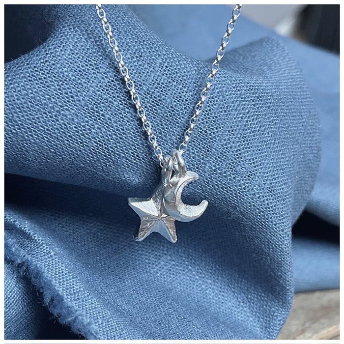 A silver pendant featuring a crescent moon and a small guiding star, hanging from a silver chain on a blue textured background.