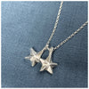 A silver pendant featuring two guiding stars charms attached to a small chain, displayed against a blue background.