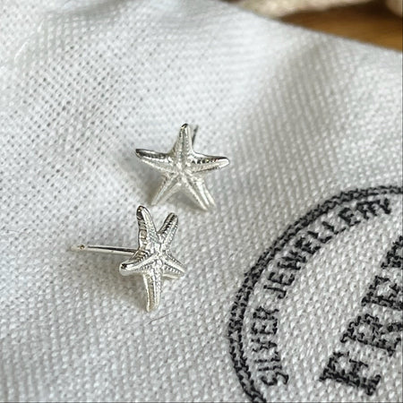 Starfish stud earrings made from sterling silver sitting on a white linen bag