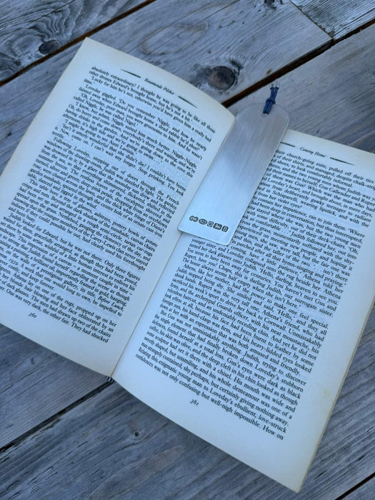 An open book spread on weathered grey wooden planks, with a white rectangular bookmark featuring the a large Hallmark.