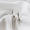 Sterling silver hoops with a textured disc on each, laying on a white linen background