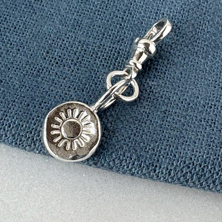 Silver charm with sun design on a textured blue and gray background