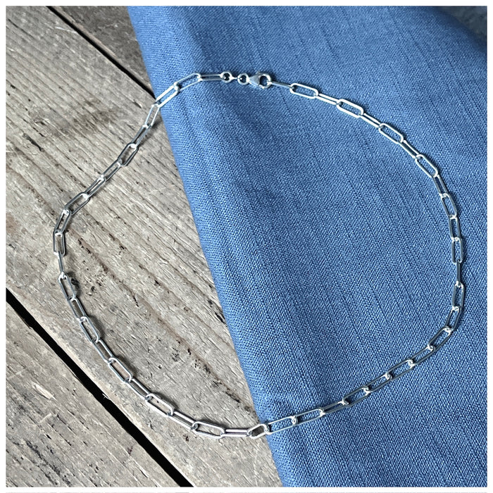 Simple trace chain necklace on a wooden background with a blue linen material on top