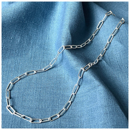 Simple trace chain necklace on a wooden background with a blue linen material on top