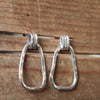 Pair of silver hoop earrings on a wooden surface with textured hoops