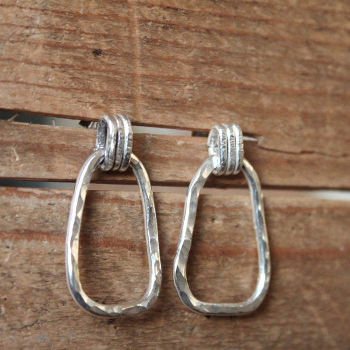 Pair of silver hoop earrings on a wooden surface with textured hoops