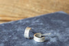 Silver hoop earrings on a dark fabric surface with a wooden background