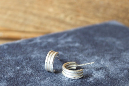 Silver hoop earrings on a dark fabric surface with a wooden background