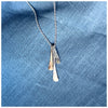 A silver pendant with three separate elements, in silver and gold hanging from a silver chain, displayed against a blue fabric background.