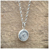A silver belcher chain necklace hanging with a stamped sunshine design, displayed against a wooden background.