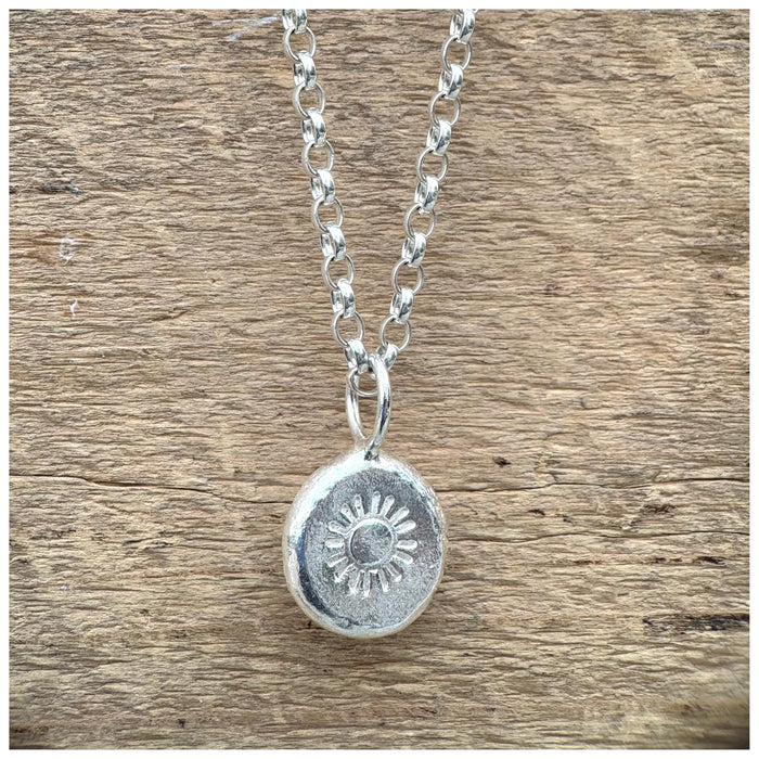 A silver belcher chain necklace hanging with a stamped sunshine design, displayed against a wooden background.