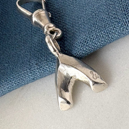 Silver voyager charm on a blue and white fabric background