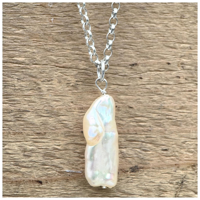 A silver belcher chain necklace with a white/silver stick pearl, displayed against a wooden background.