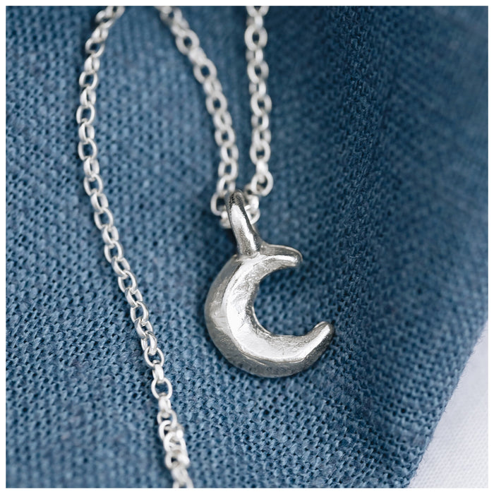 A silver crescent moon pendant on a chain, displayed against a blue textured background.