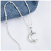 A silver crescent moon pendant attached to a small satellite chain, displayed against a blue textured background