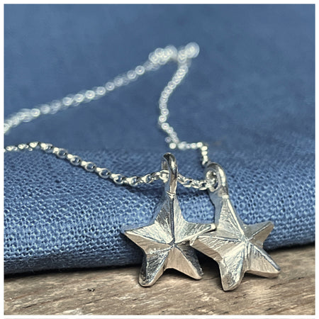 A silver pendant featuring two guiding stars charms attached to a small chain, displayed against a blue background.