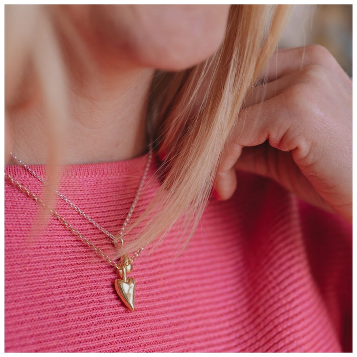 A 9ct gold heart-shaped pendant necklace worn on top of a pink jumper