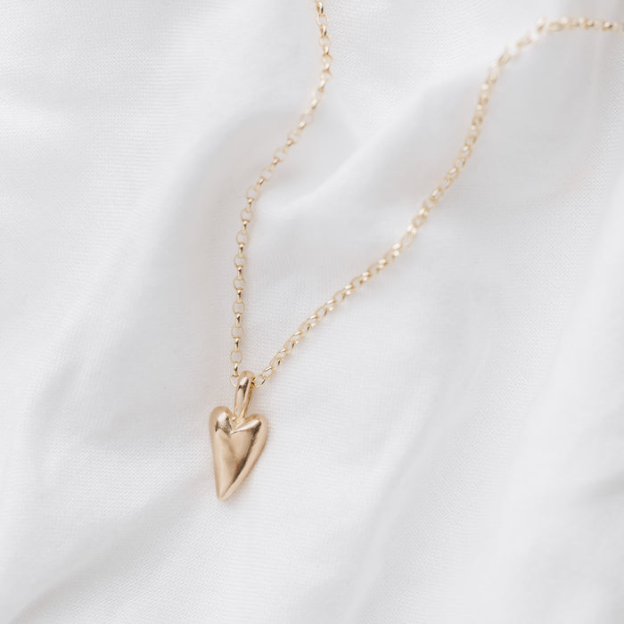 A gold heart-shaped pendant necklace laid out on a white surface.