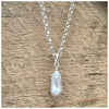 A silver belcher chain necklace with a grey stick pearl, displayed against a wooden background.